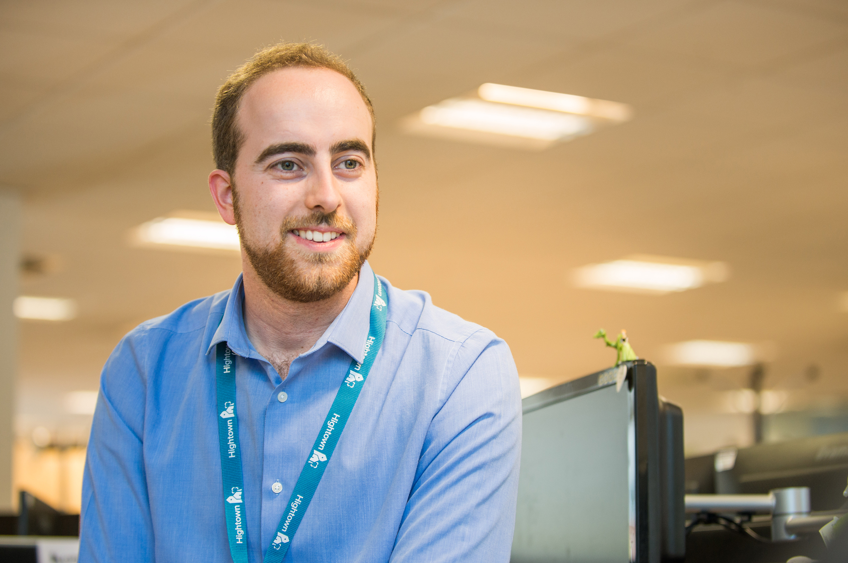 Staff member sat down, looking at the camera, smiling. He is wearing a light blue shirt. 