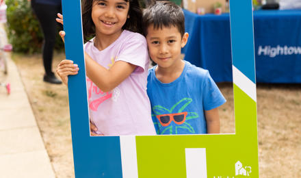 Two young children holding up a cardboard cut out of a house, which reads 'building homes. Supporting people'.