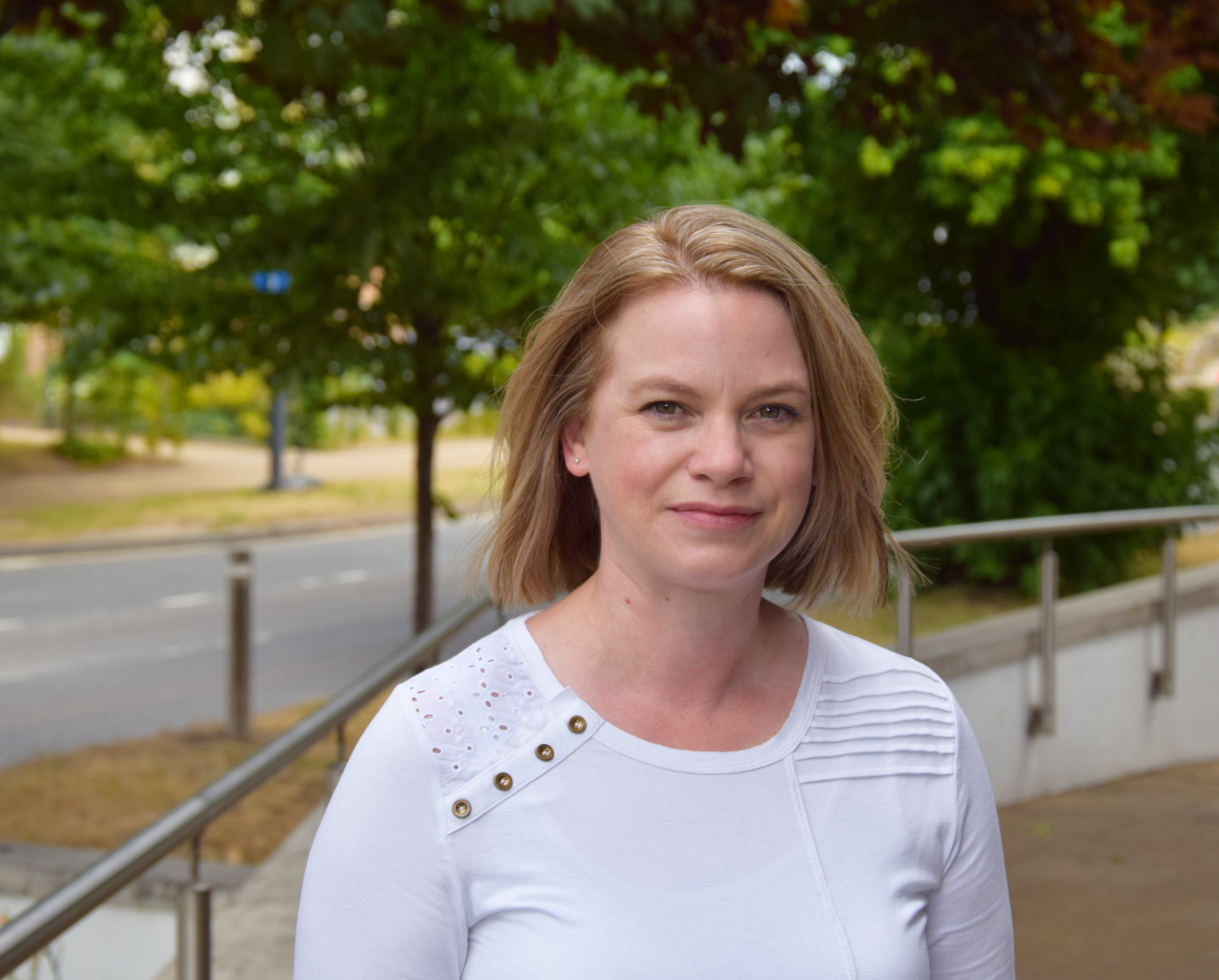 Director of housing. She is wearing a white t-shirt and has shoulder length blonde hair and green eyes. 