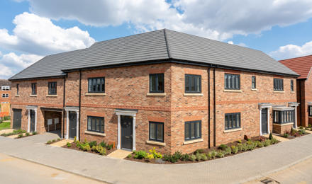 A block of houses with some small bushes outside. Brick work with black windows. 