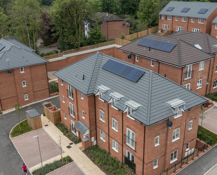 An aerial photo of new build flats and houses, with solar panels on the roof and parking spaces outside the properties. 