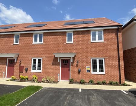 Front view of the property which has a red front door and landscaped planting