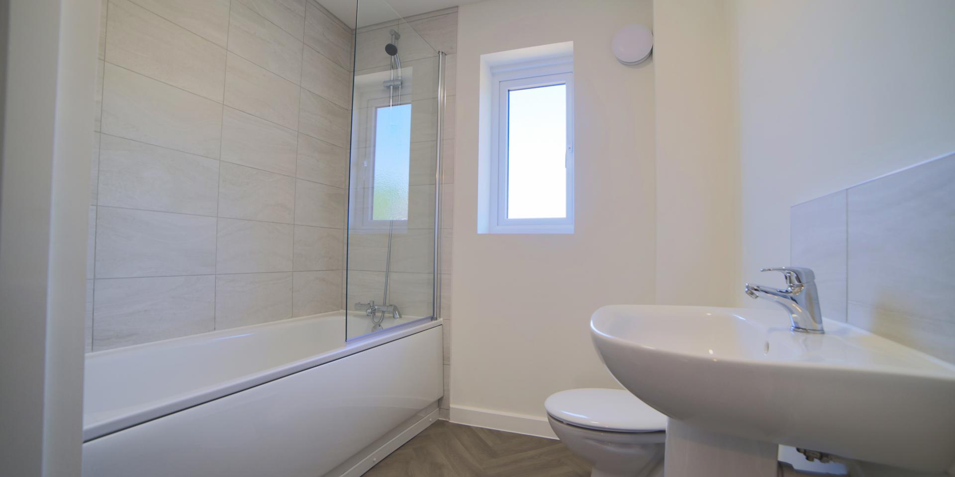 The bathroom has a white suite with a shower over the bath and fitted glass shower screen. There is also a built-in storage cupboard.