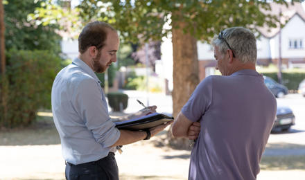A member of staff is stood outside taking notes whilst talking to a resident