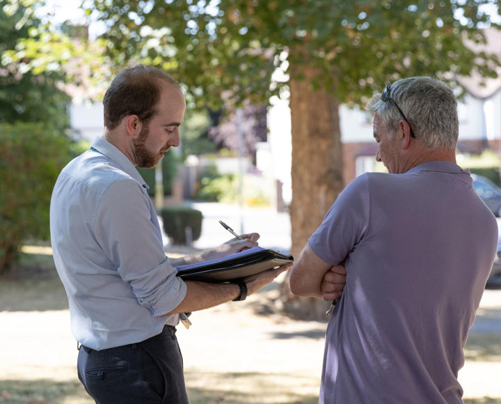 A member of staff is stood outside taking notes whilst talking to a resident