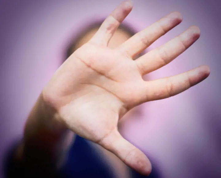 A person holding the palm of their hand up to the screen. The hand is also covering their face. 