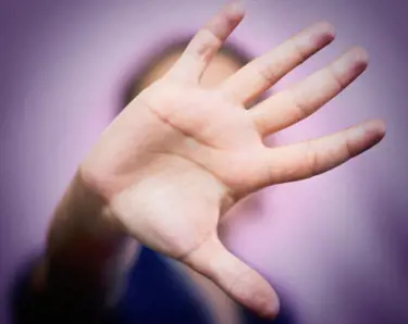 A person holding the palm of their hand up to the screen. The hand is also covering their face. 