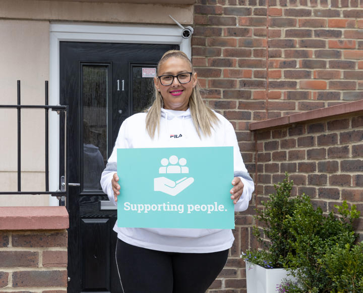 A resident is holding a Hightown sign that says 'supporting people' and has a symbol of a hand holding up three people.
