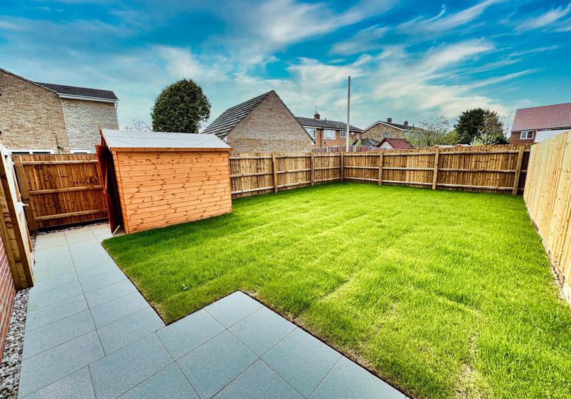 The turfed rear garden with patio area and shed