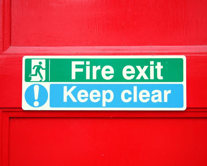 A fire exit and keep clear sign on a red door.