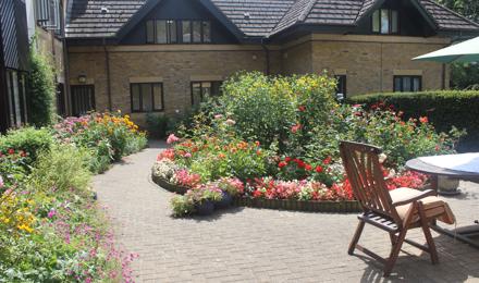 Outside front garden of flats, with a table and chairs and lots of colourful flowers planted.