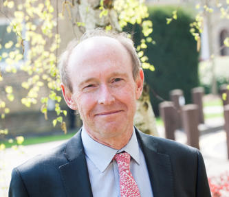 CEO of Hightown. He is wearing a dark grey suit, blue shirt and a red and white patterned tie. 