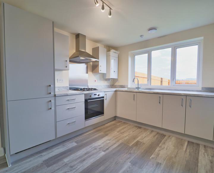 Light grey kitchen units with integrated appliances and an electric oven, gas hob and stell cooker hood and splash back