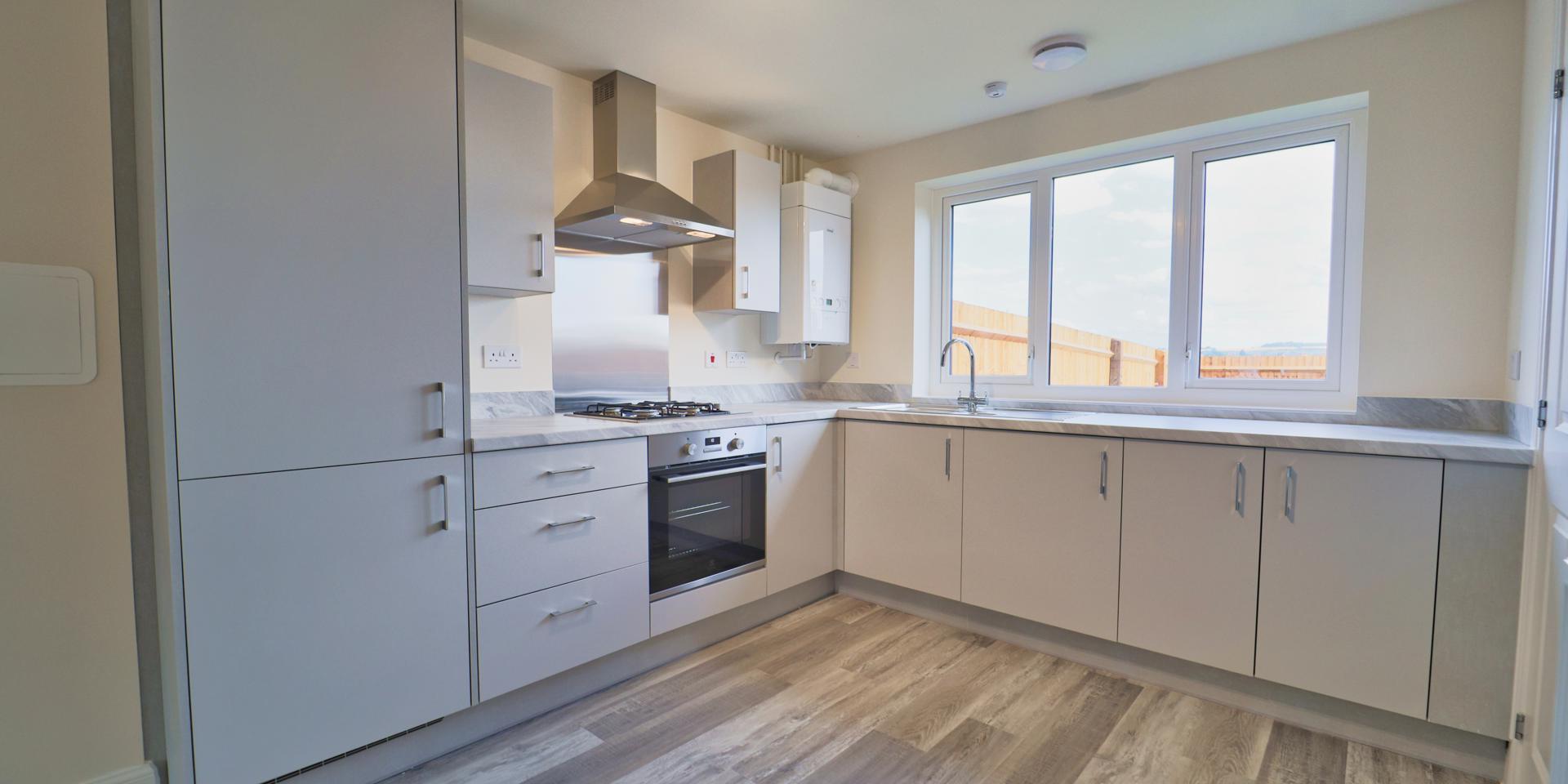 Light grey kitchen units with integrated appliances and an electric oven, gas hob and stell cooker hood and splash back