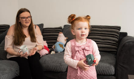 Hightown resident and her daughter who is holding a foam toy house, on the sofa, in their new home.