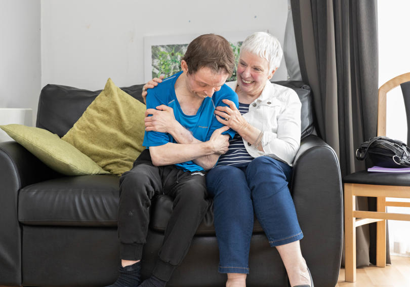 A service user and his mum sitting on a sofa together smiling