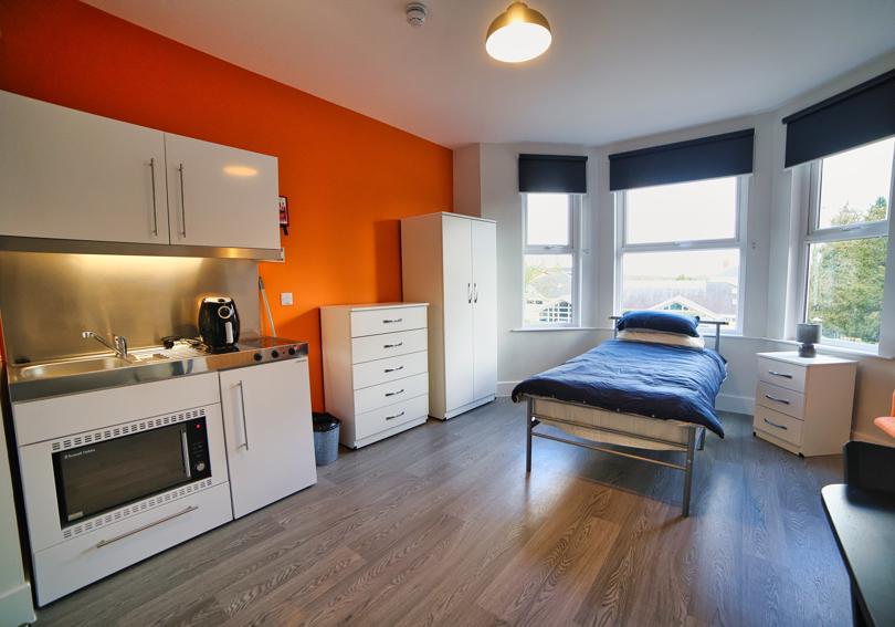 Studio flat with a bed, kitchenette, furniture and bright orange wall