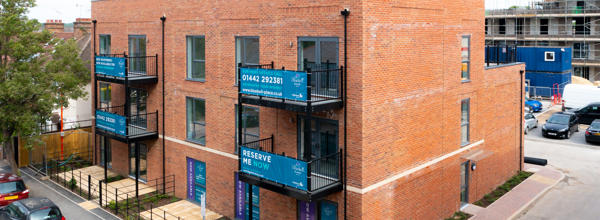 A new block of flats, 3 floors high. 4 have black metal balconies. 