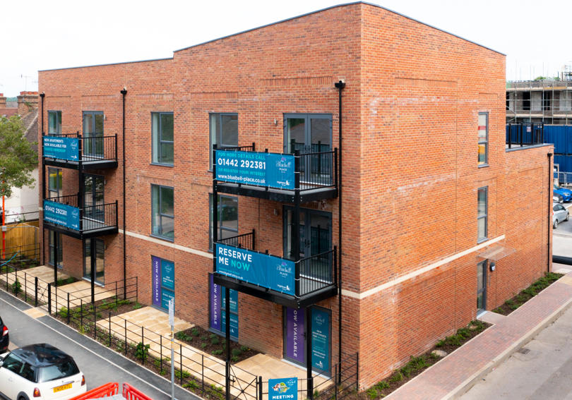 A new block of flats, 3 floors high. 4 have black metal balconies. 