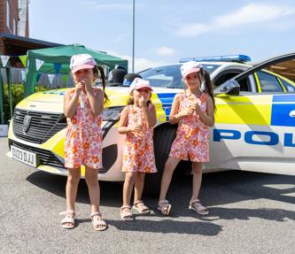 Three young children, stood in front of a police car on a sunny day, for a resident involvement open day.