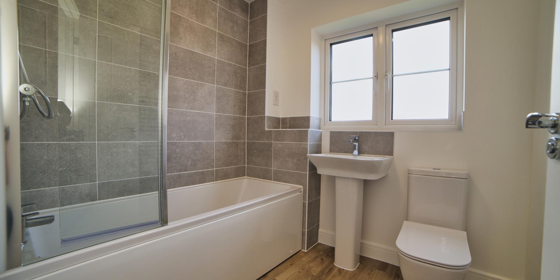 The bathroom has white suite with a shower over the bath and glass shower screen