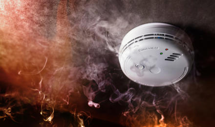 A smoke detector on a ceiling surround by smoke from a fire