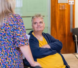 A man in a yellow tshirt and blue hoody, smiling, looking up at a woman in a colourful dress