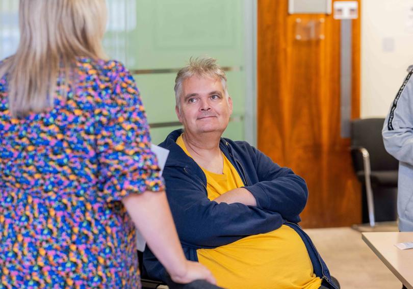 A man in a yellow tshirt and blue hoody, smiling, looking up at a woman in a colourful dress