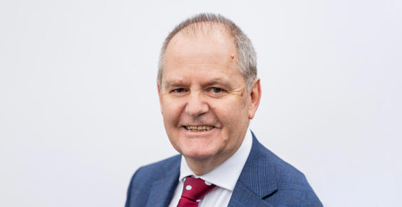 A headshot of the director of finance, David Skinner, smiling at the camera. He is wearing a blue blazer, white shirt and a red and white dotted tie.