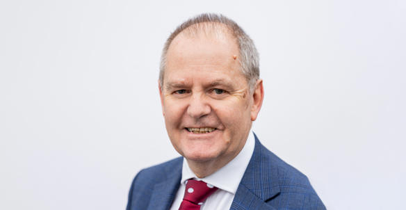 A headshot of the director of finance, David Skinner, smiling at the camera. He is wearing a blue blazer, white shirt and a red and white dotted tie.