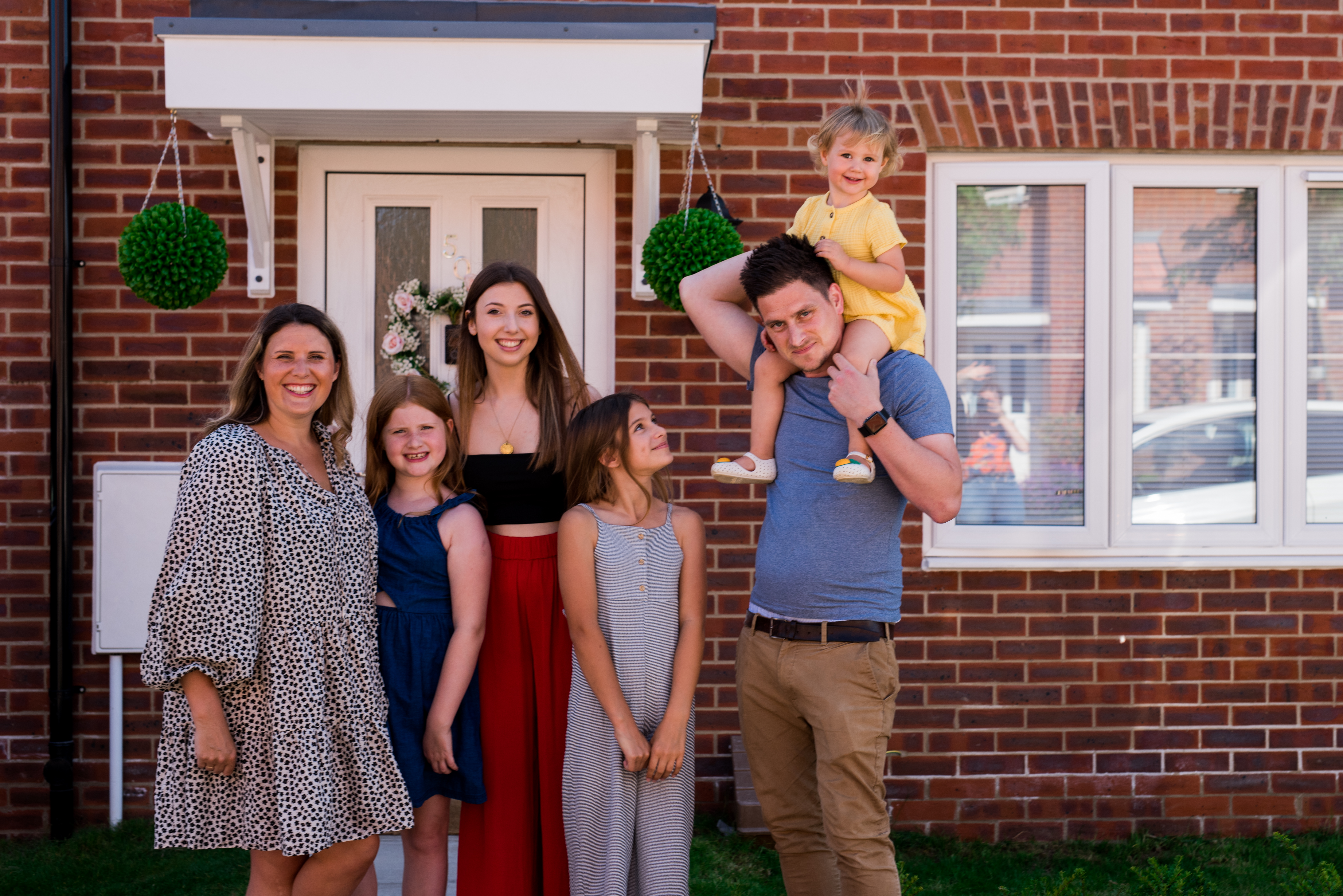 A family standing outside their new Hightown property, smiling and looking happy.