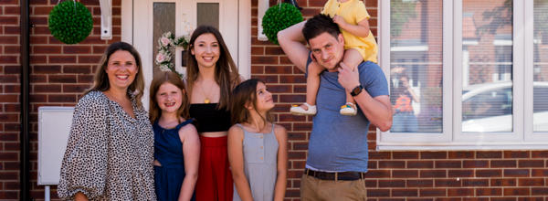 A family standing outside their new Hightown property, smiling and looking happy.