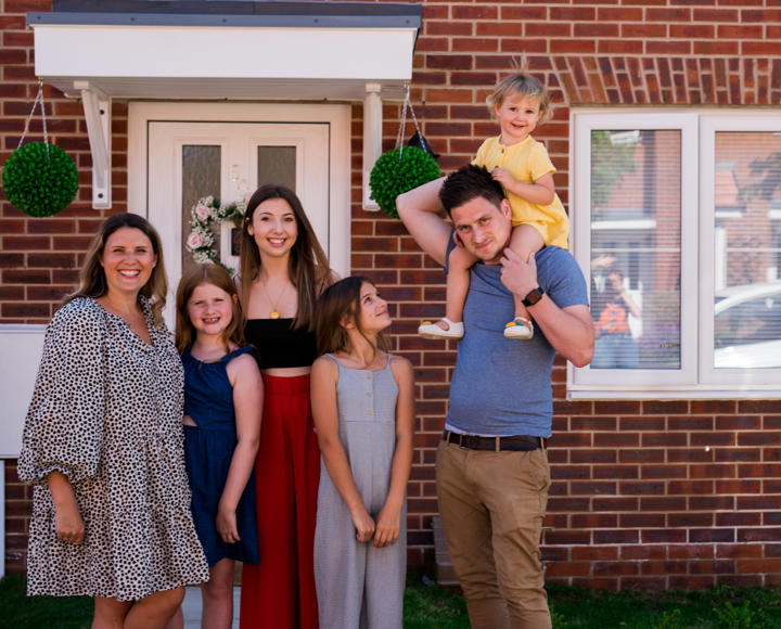 A family standing outside their new Hightown property, smiling and looking happy.